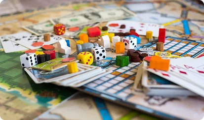 Verschillende elementen van bordspellen, zoals kaarten, fiches en dobbelstenen, liggen verspreid over het speelbord.